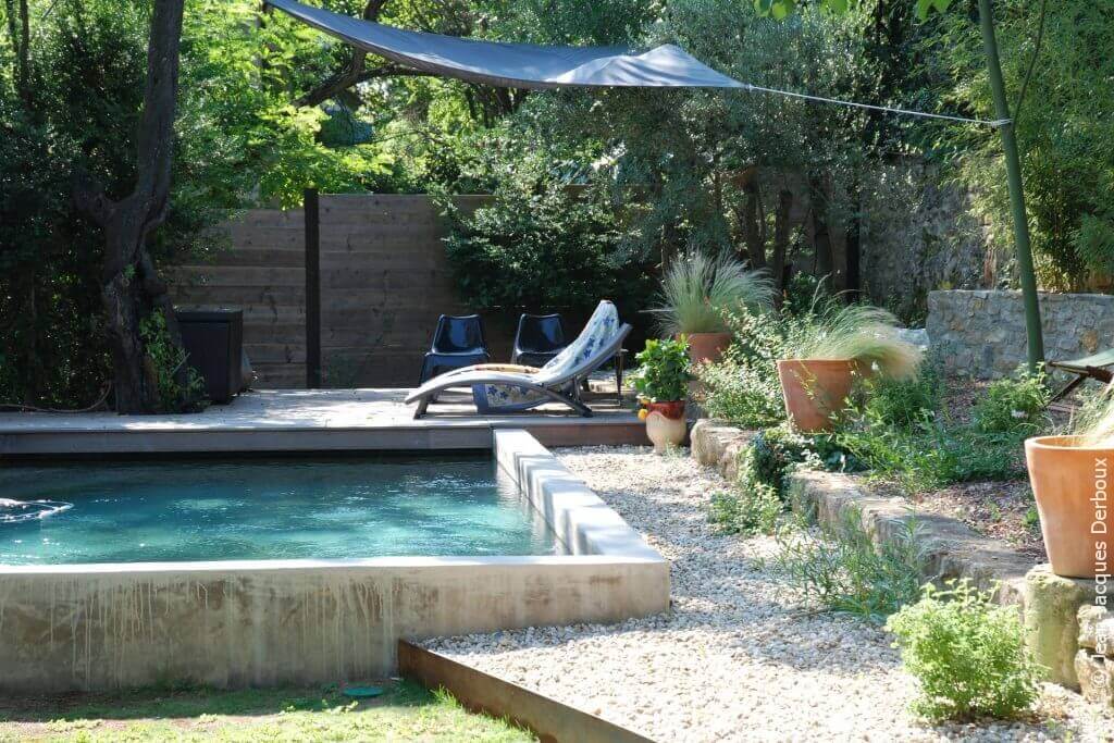 Piscine maçonnée, enduit ciment, terrasse bois, mobilier, bain de soleil, ombrage toile, pots décoratifs.