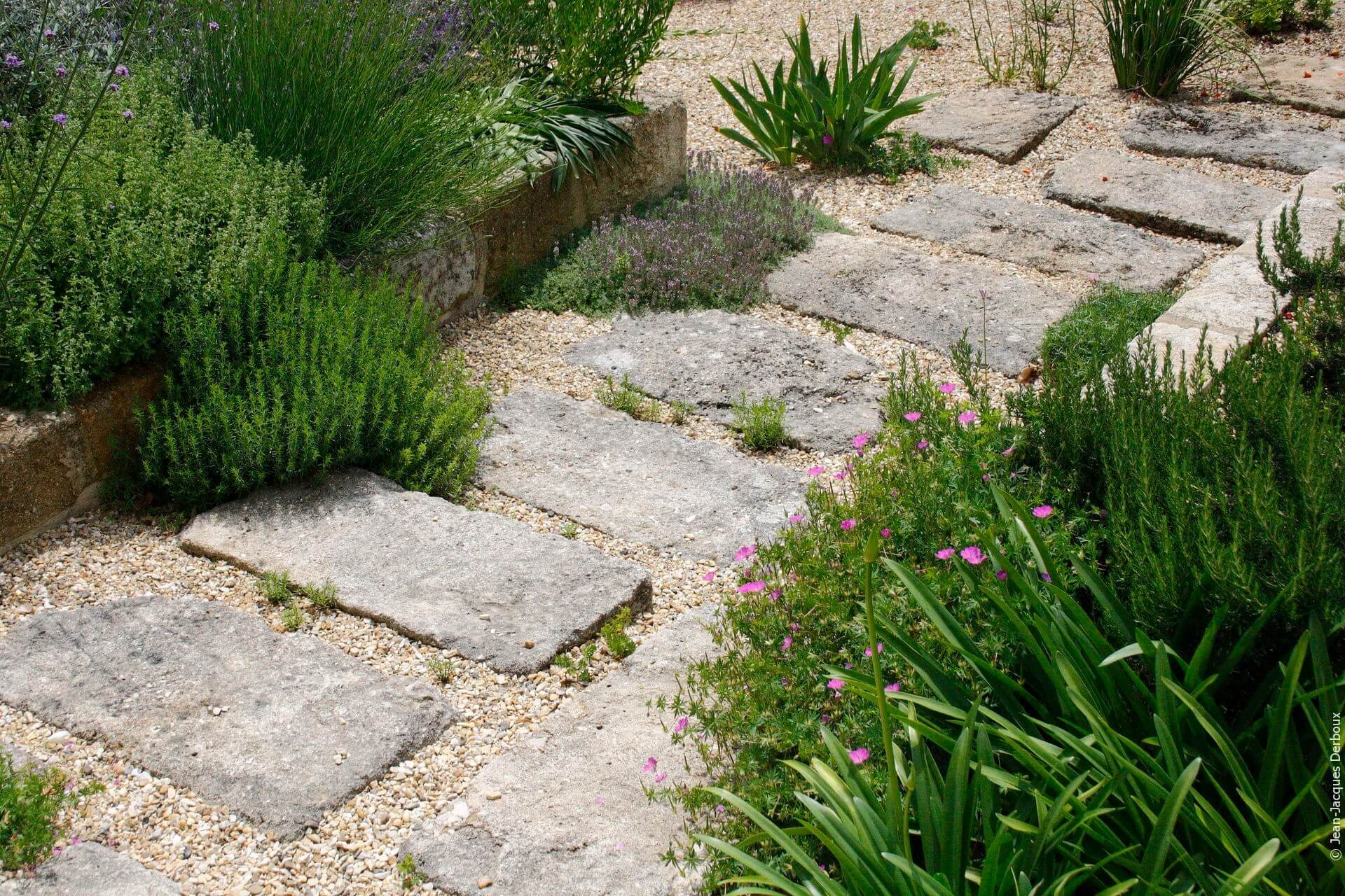 Cour de maison de village, dalle en pierre taillée, gravier, jardinière en bloc pierre taillée, plantes de jardin sans arrosage.