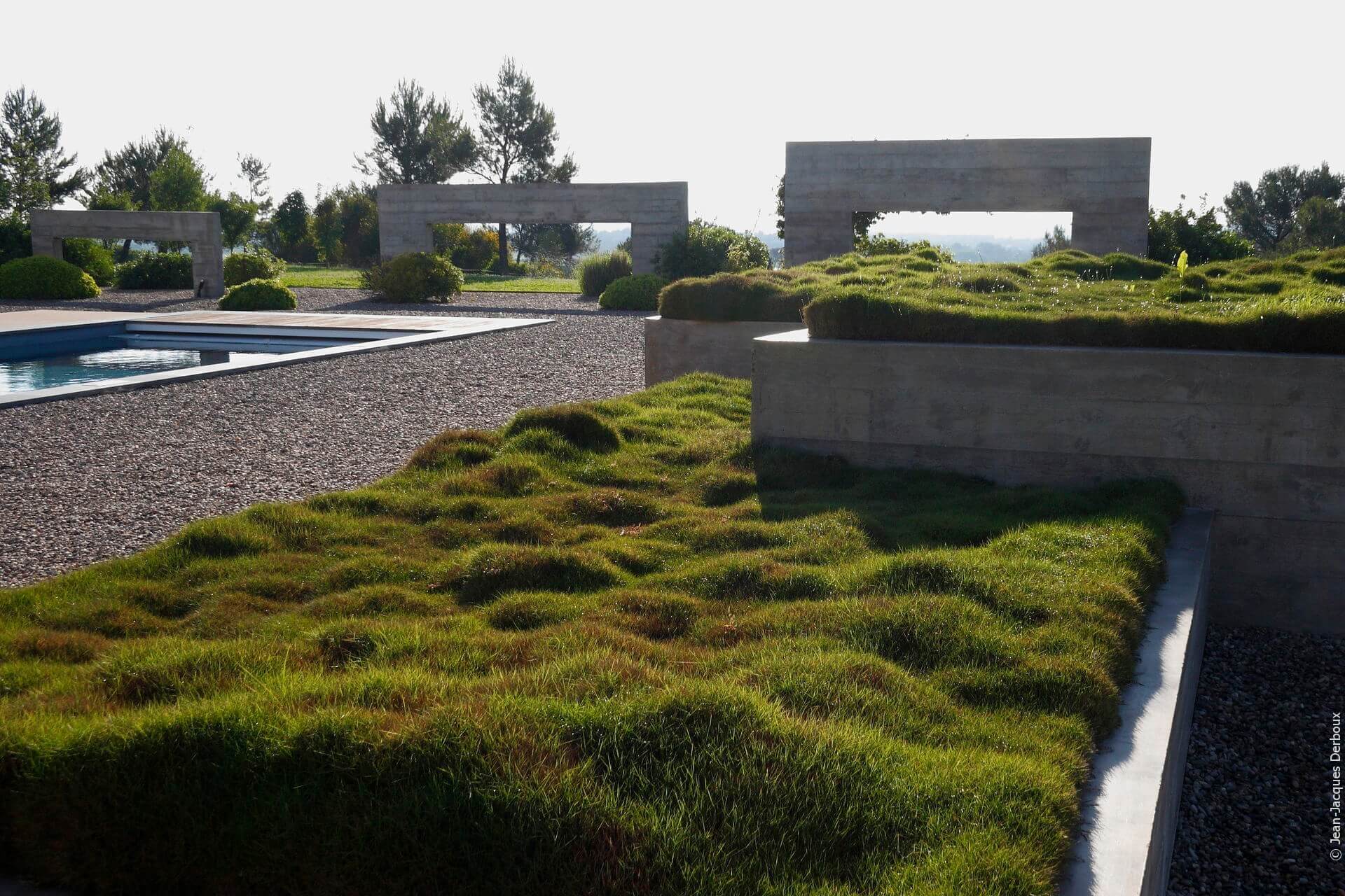 Abord piscine, jardin sur gravier, structure décorative en béton, contemporain, grande jardinière plantée de zoysia