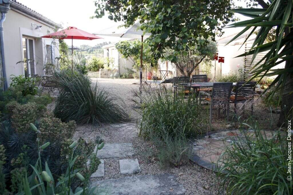 Jardin du sud, courette du Languedoc, à l’ombre des parasols et des arbres, mobilier de jardin, gravier, jardin écologique, dalle en pierre dans gravier, figuier.