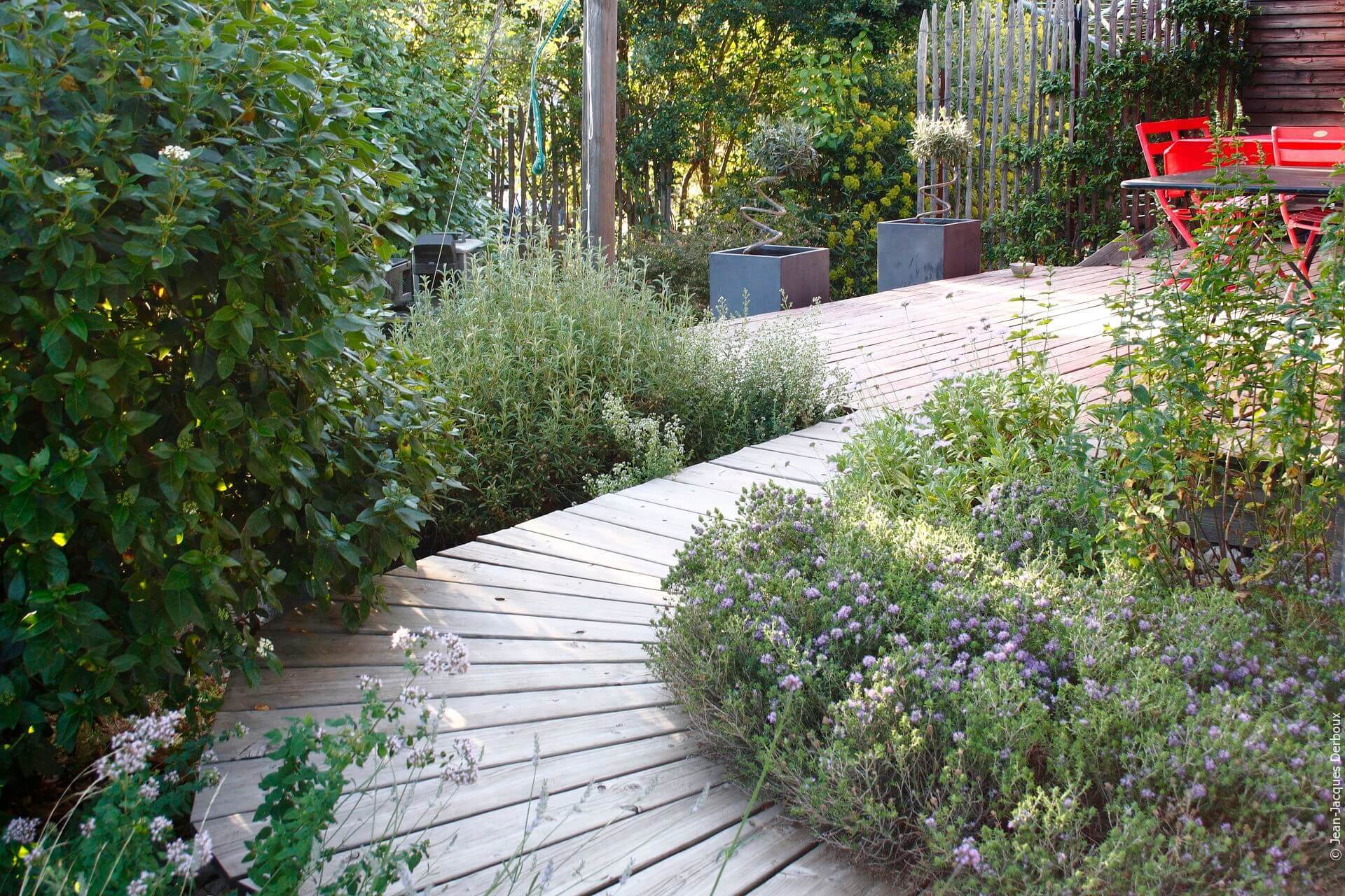 Terrasse en bois, ponton e, bois, pots en métal, mobilier rouge, jardin sec et aromatique.